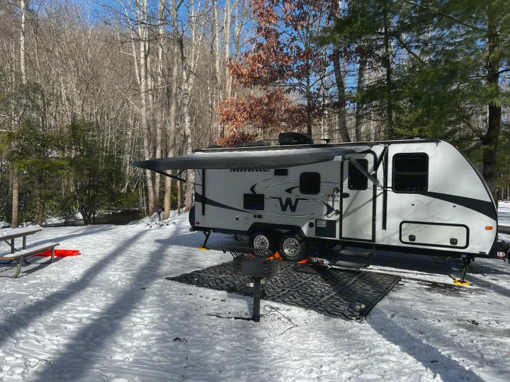 RV rental set up for winter camping in a snowy forest. Features a grill, picnic table, and extended awning.. Winnebago Micro Minnie 2306BHS 2019