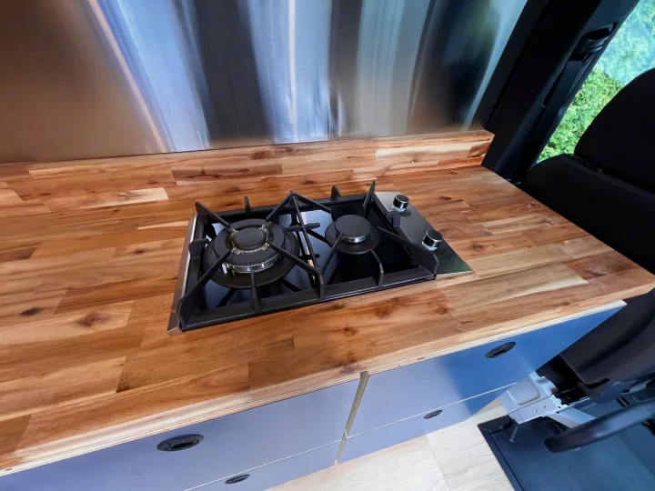 Modern RV rental kitchen featuring a built-in gas stove, warm wood countertop, and sleek cabinets.. Mercedes Sprinter 2024