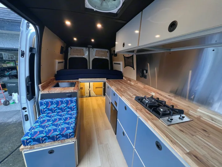 This modern van conversion rv rental features a compact kitchen with wood counters, a bed, and vibrant seating.. Mercedes Sprinter 2024