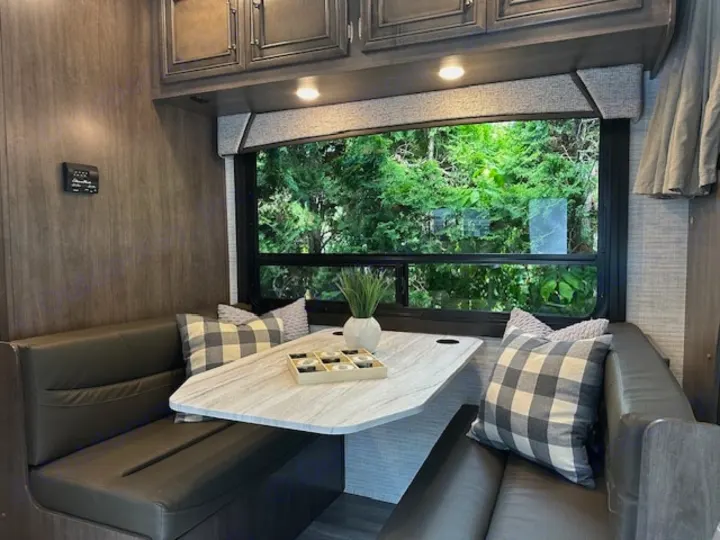 Cozy modern RV rental dinette with booth seating, sleek table, and large window showcasing nature views for comfortable travel.. Entegra Coach Odyssey SE 22C 2024