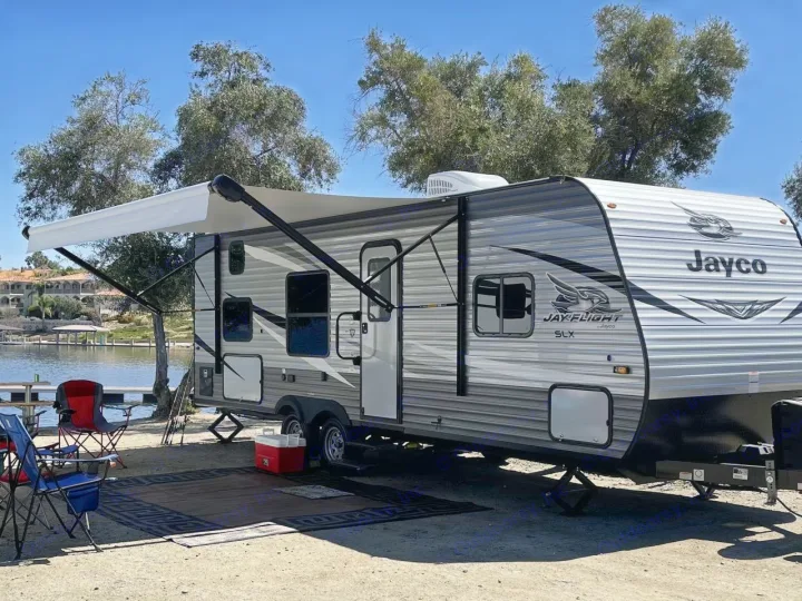 This Jayco travel trailer, a great RV rental option, is set up for lakeside camping with its awning extended and chairs out.. Jayco Jay Flight SLX 2021