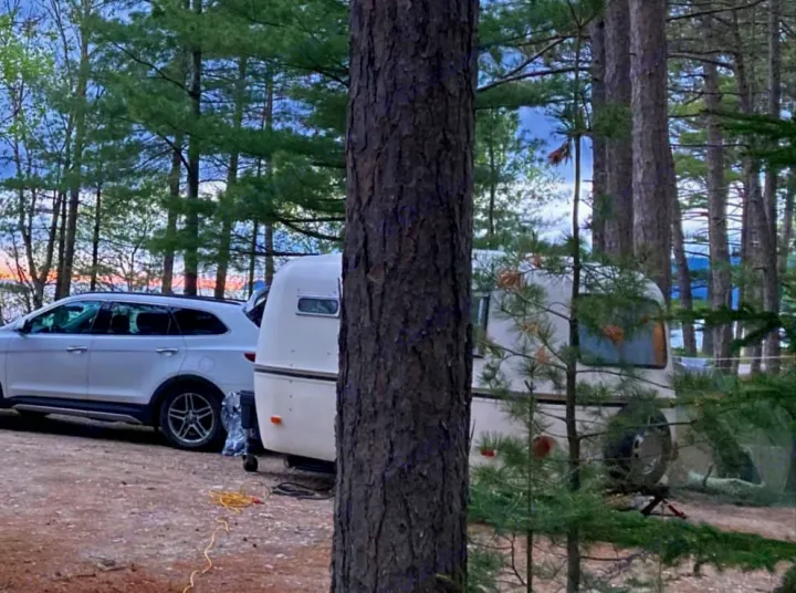 White camper, an RV rental, and SUV at a lakeside campsite among tall pines. Ideal for nature trips.. Boler B13 1973