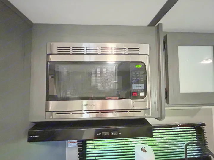 RV rental kitchen: A stainless steel over-the-range CONTOURE microwave sits above a GREYSTONE hood, typical of RV appliances.. Dutchmen Aspen Trail LE 2022