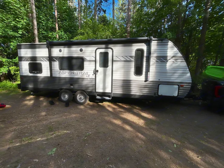 An Aspen Trail travel trailer, perfect for an RV rental, parked at a sunny, wooded campsite for an outdoor adventure.. Dutchmen Aspen Trail LE 2022