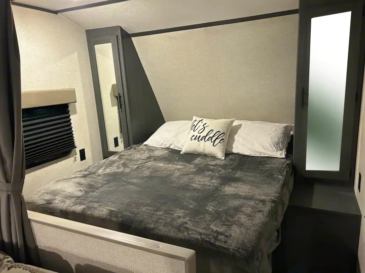 Cozy RV rental bedroom with a comfy full bed, gray bedding, built-in mirrored wardrobes, and light-textured walls.. Dutchmen Aspen Trail LE 2022