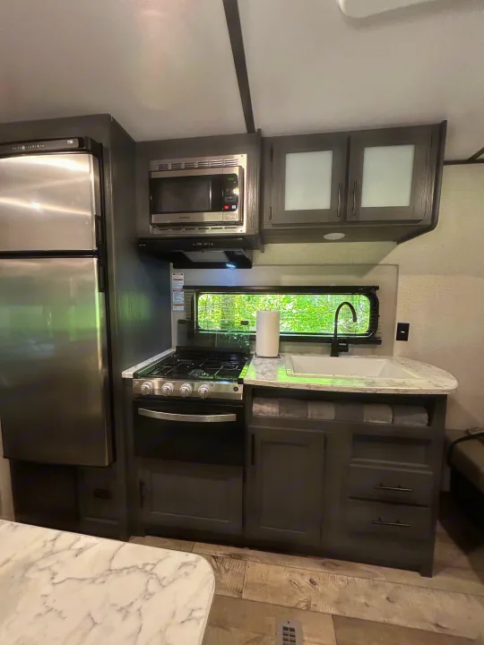 Well-equipped RV rental kitchen with stainless steel fridge, microwave, stove, sink, gray cabinets, and marble counters.. Dutchmen Aspen Trail LE 2022