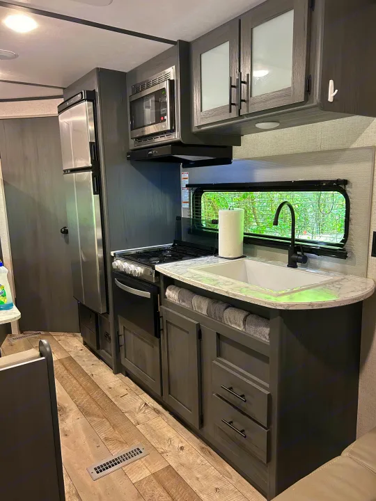 Inside a comfortable RV rental: modern kitchen with stainless appliances, grey cabinets, and a scenic window view.. Dutchmen Aspen Trail LE 2022