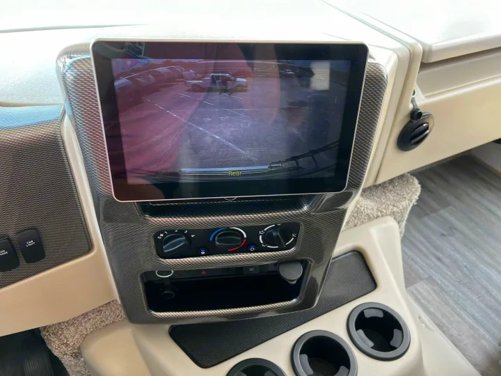 RV rental interior: Dashboard with a large rearview monitor showing a parking lot, climate control panel, and cup holders.. Thor Motor Coach A.C.E 2024