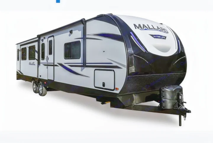 A white, black, and gray Mallard travel trailer, perfect for RV rental trips. Features multiple windows, doors, and a front hitch.. Heartland RVs Mallard 2021