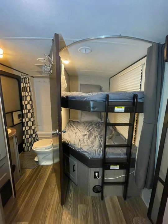 RV rental interior showing bunk beds with gray bedding and a compact bathroom with patterned shower.. Heartland RVs Mallard 2021