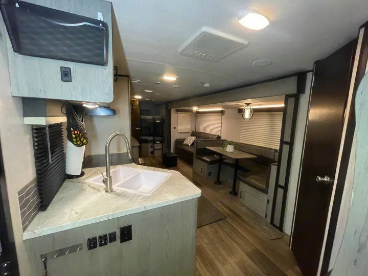 RV rental interior: Bright, modern kitchen with sink, dining booth, comfortable sofa, and bunk beds for a full living experience.. Heartland RVs Mallard 2021