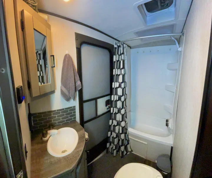 This efficient RV rental bathroom features a compact sink, toilet, and shower with a geometric shower curtain.. Heartland RVs Mallard 2021