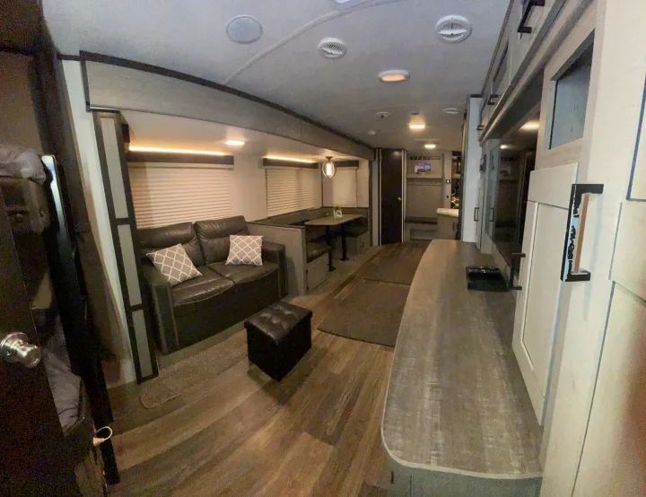 RV rental interior: A modern living and dining area with a dark sofa, booth seating, and wood-look flooring.. Heartland RVs Mallard 2021