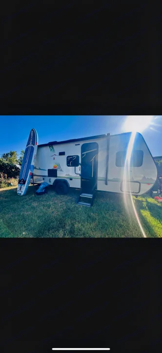 Perfect RV rental for outdoor fun! White camper with paddleboard on grass, bright sun, clear blue sky.. No Boundaries 19.8 2021
