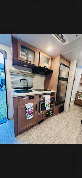 Explore this compact RV rental kitchen featuring a sink, stovetop, microwave, and fridge within wood cabinetry.. No Boundaries 19.8 2021