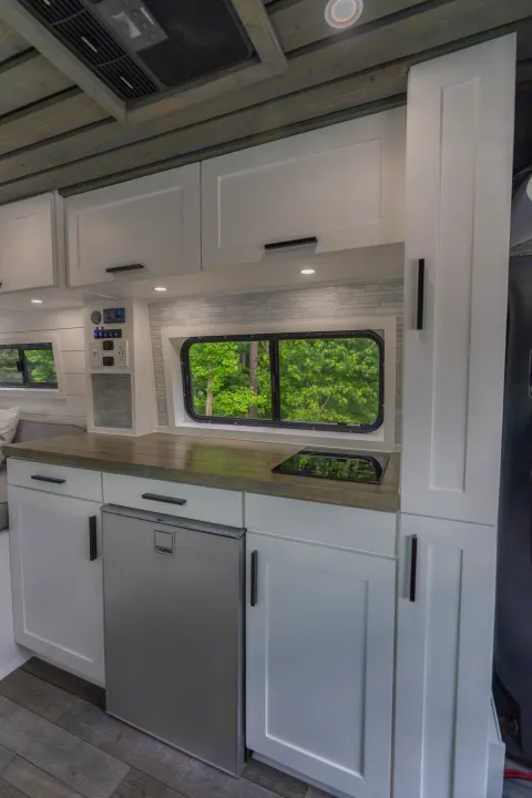 Driver side kitchen area includes pantry, spice drawer, butcher block countertop, built-in induction cooktop, fridge w/ mini freezer, slide-out prep area, sliding window, overhead cabinet and galley storage, and control center. Mercedes-Benz Sprinter 2020