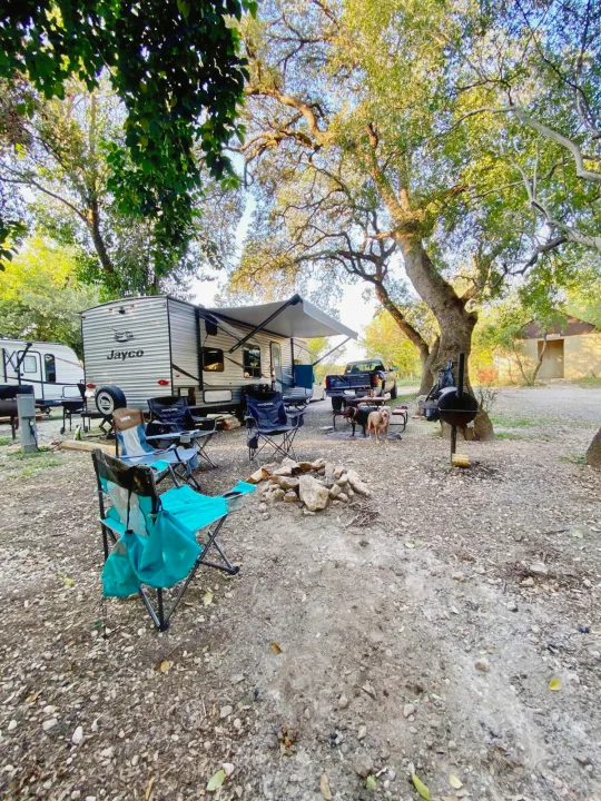Perfect RV rental camping setup: A Jayco travel trailer with awning, chairs, fire pit, grill, and dogs under trees.. Jayco Jay Flight SLX 2020
