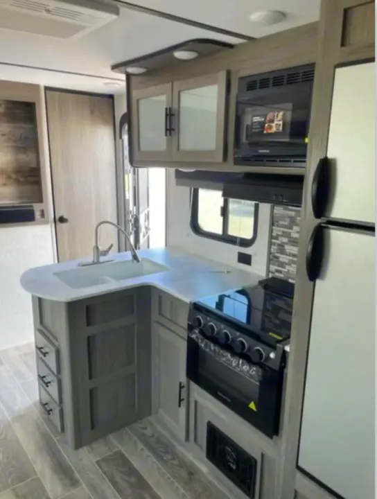 Modern RV rental kitchen featuring a sink, stove, microwave, and fridge for comfortable travel.. Gulf Stream Ameri-Lite 2022