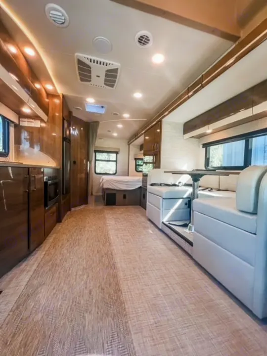 Explore this modern RV rental interior, featuring a kitchen, bedroom, and dining area with bright lighting and wood accents.. Entegra Coach Qwest 24L 2024