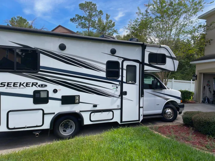 Bright white Forest River Seeker RV, ideal for your next rv rental, parked in a sunny residential driveway.. Forest River Sunseeker LE 2023