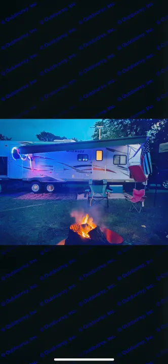 Cozy night at an RV rental site with a Wildwood travel trailer illuminated by blue lights & a warm campfire.. Forest River Wildwood 2012