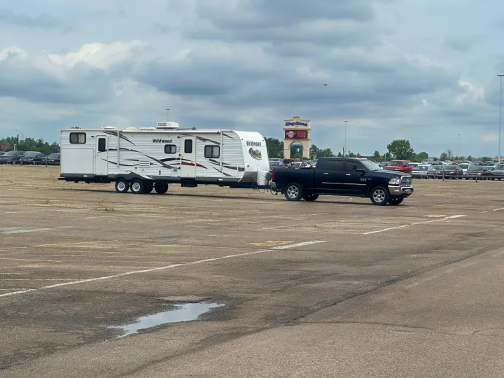 Black truck towing a white Wildwood travel trailer (RV rental) in an empty Kings Island lot.. Forest River Wildwood 2012
