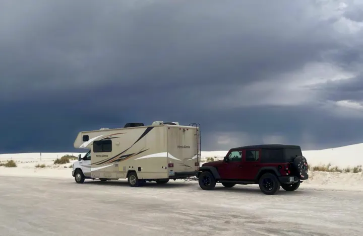 An RV rental (Minnie Winnie) tows a red Jeep Wrangler at White Sands National Park under dramatic, stormy skies.. Winnebago Minnie Winnie 2018