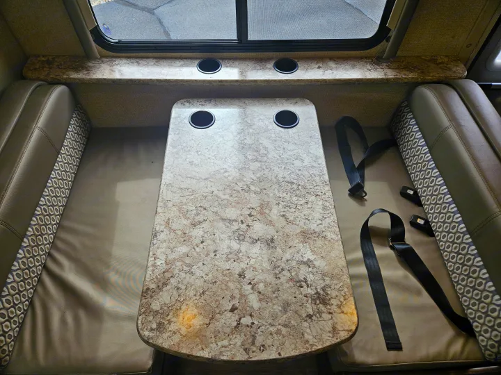 RV rental dinette shows a marbled table with cup holders, two benches, and seatbelts for travel safety.. Thor Freedom Elite 2018