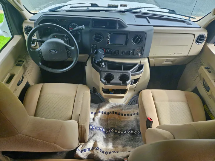 Ford RV rental cockpit showing dashboard, steering wheel, driver/passenger seats, and central console with cup holders.. Thor Freedom Elite 2018