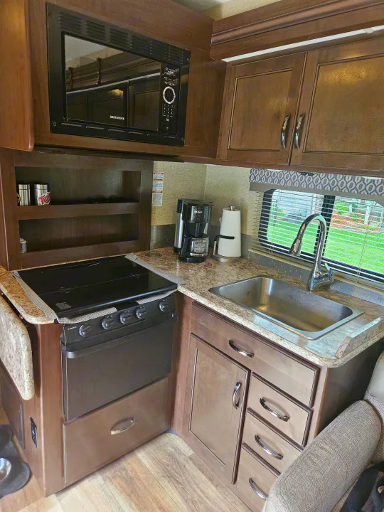 RV rental kitchen: compact with microwave, stove, sink, coffee maker, and wood-toned cabinets/drawers.. Thor Freedom Elite 2018