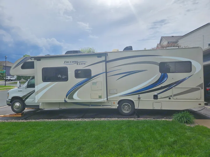 Tan Freedom Elite Class C RV rental, parked on a driveway with front wheels on leveling blocks, ready for your next adventure.. Thor Freedom Elite 2018