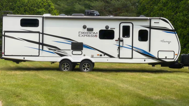 White travel trailer RV rental, Freedom Express model, parked on green grass. Perfect for your next adventure.. Coachmen 292BHDS FREEDOM EXPRESS LIBERTY EDITION 2022