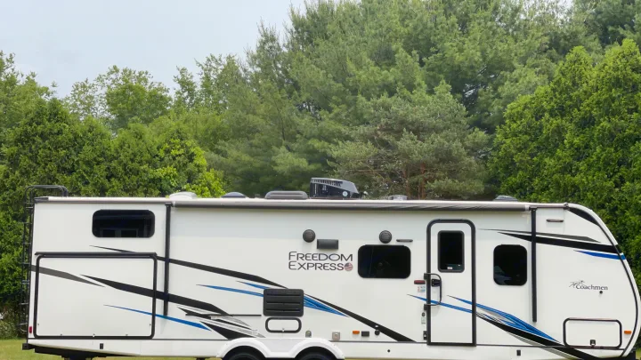 White Coachmen Freedom Express RV rental side view, showing windows, door, and roof equipment, parked outdoors.. Coachmen 292BHDS FREEDOM EXPRESS LIBERTY EDITION 2022