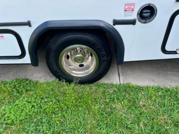 Side view of an RV rental, featuring its large tire, chrome wheel, and gasoline tank with a "GASOLINE ONLY" warning.. Forest River Sunseeker LE 2023