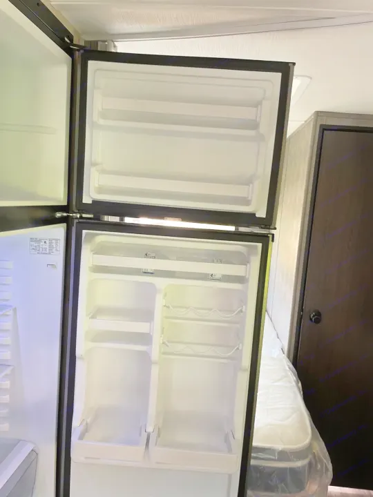 Compact RV rental refrigerator open inside a camper, showing empty shelves and freezer compartments.. Forest River Sunseeker LE 2023