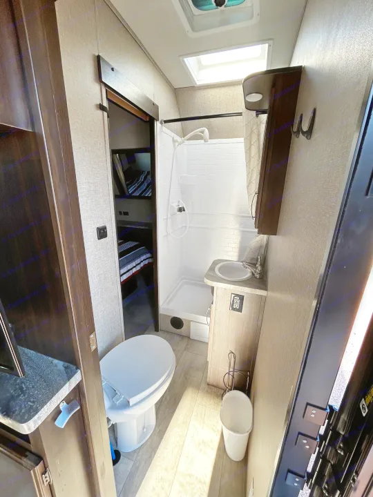 Compact RV rental bathroom features a white toilet, shower, and sink, with light walls and wood-look flooring.. Grand Design Momentum 2020