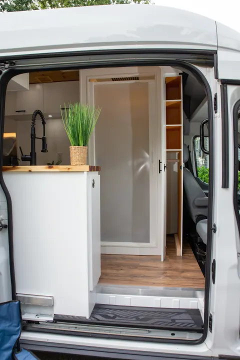 RV rental camper van interior: kitchen with sink, plant, and custom storage visible through the open side door.. Ford Transit 2018