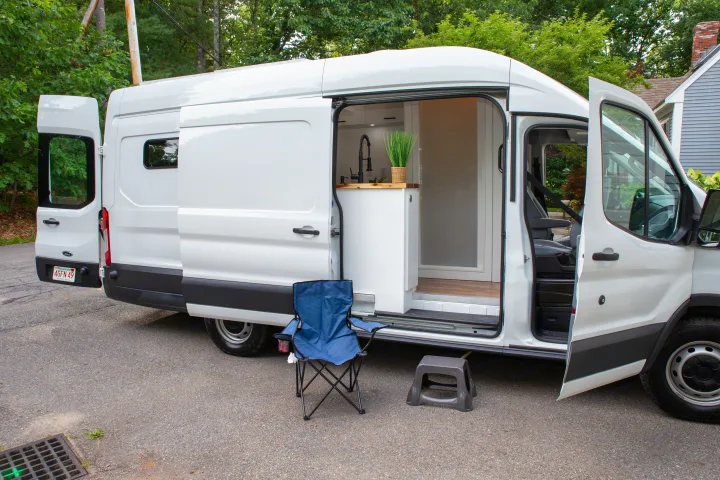 A white converted Ford Transit camper van, an ideal RV rental, with doors open revealing a modern kitchen setup.. Ford Transit 2018