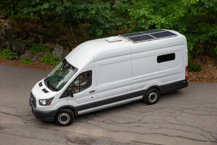 White camper van with solar panels seen from above. Driver waves. Perfect for an RV rental adventure.. Ford Transit 2018