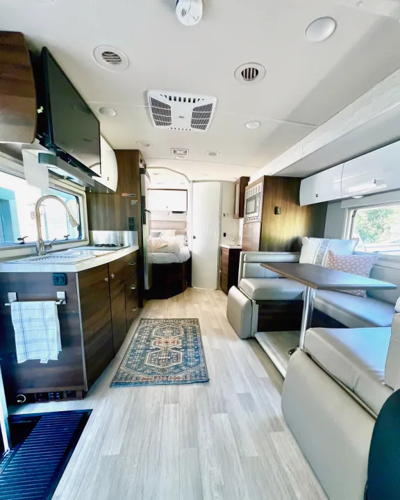Bright RV rental interior, showing kitchen with sink, cozy dinette, and a comfy bed at the rear.. Winnebago View 2022