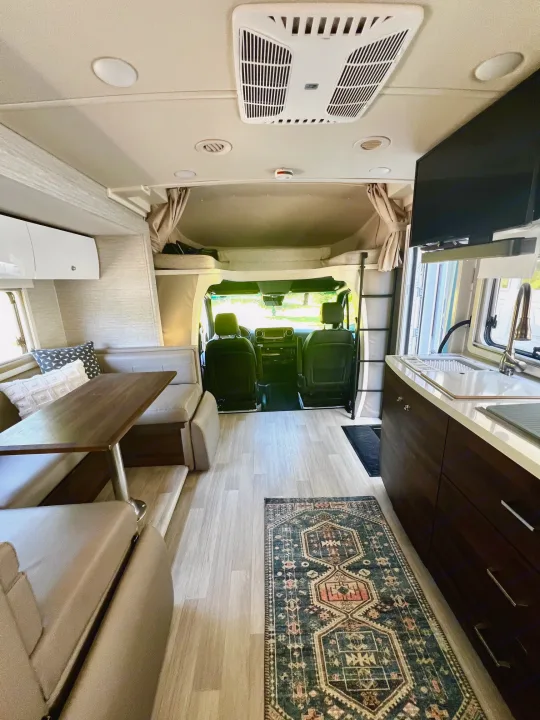 Cozy RV rental interior with modern kitchen, dining area, overhead bunk, and front cab view.. Winnebago View 2022