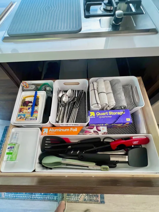 An RV rental kitchen drawer neatly organized with cutlery, cooking utensils, Purell, aluminum foil, and storage bags.. Winnebago View 2022