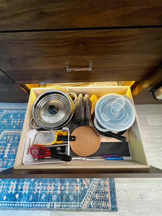 An open RV rental kitchen drawer showcases essential cookware: pots, pans, lids, and utensils, all neatly organized for easy access.. Winnebago View 2022
