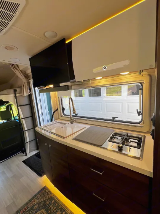 Compact RV rental kitchen with modern sink, stove, TV, and access to a sleeping loft. Perfect for travel.. Winnebago View 2022