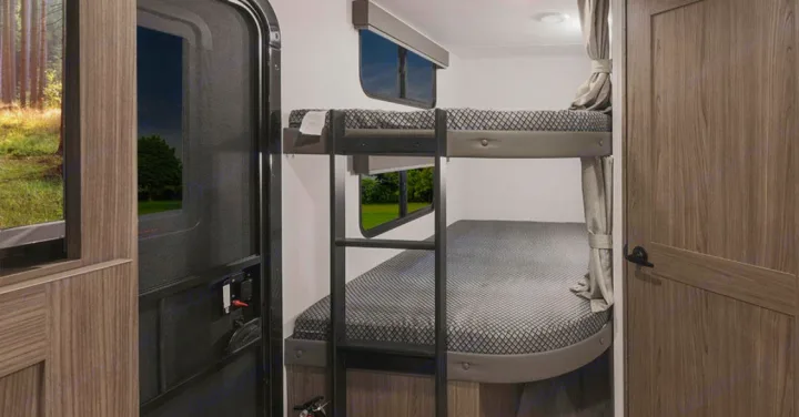 Cozy RV rental interior featuring two bunk beds with a ladder, a wooden door, and windows showing nature outside. Perfect for trips.. Alliance Delta 251BH 2024
