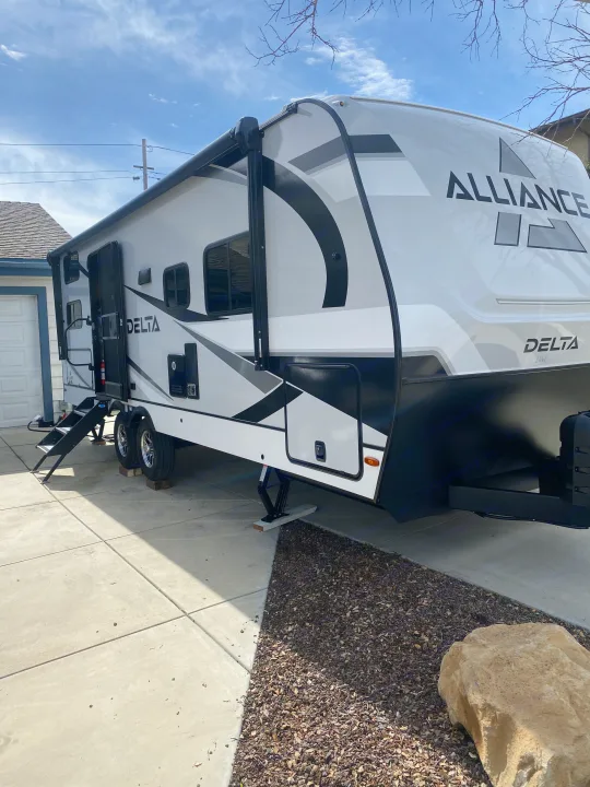 A white and black Alliance Delta travel trailer, an RV rental, parked on a concrete driveway with steps extended.. Alliance Delta 251BH 2024