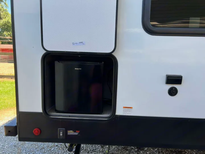 RV rental: Exterior view of a white RV with an open compartment revealing a Hotpoint outdoor mini-fridge, outlets, and controls.. Dutchmen Kodiak SE 2024