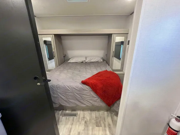 Comfortable RV rental bedroom with a grey bed, red blanket, and integrated storage, offering a cozy space for travel.. Dutchmen Kodiak SE 2024