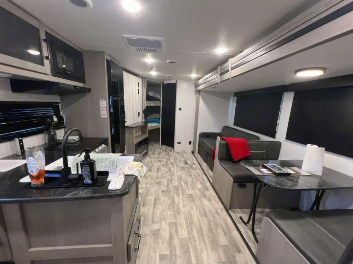 Spacious rv rental interior featuring a modern kitchen, dining area, and bunk beds with light wood tones.. Dutchmen Kodiak SE 2024