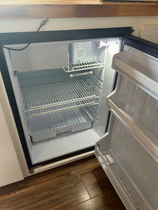Spacious, clean, and empty mini-fridge in an RV rental, with door open revealing shelves, ready for your travel provisions.. Ford Transit 2018